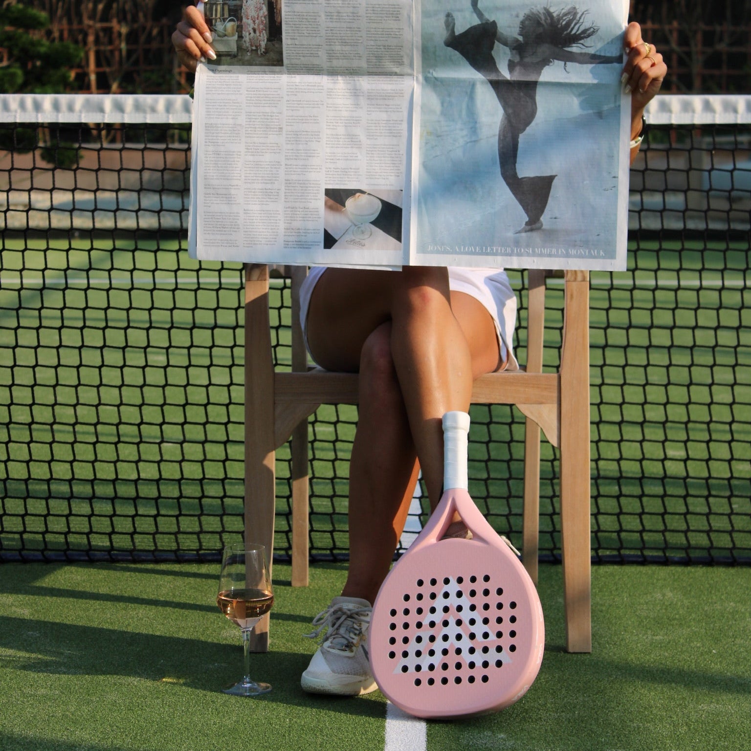 Person holding a newspaper on a tennis court with a pink paddle