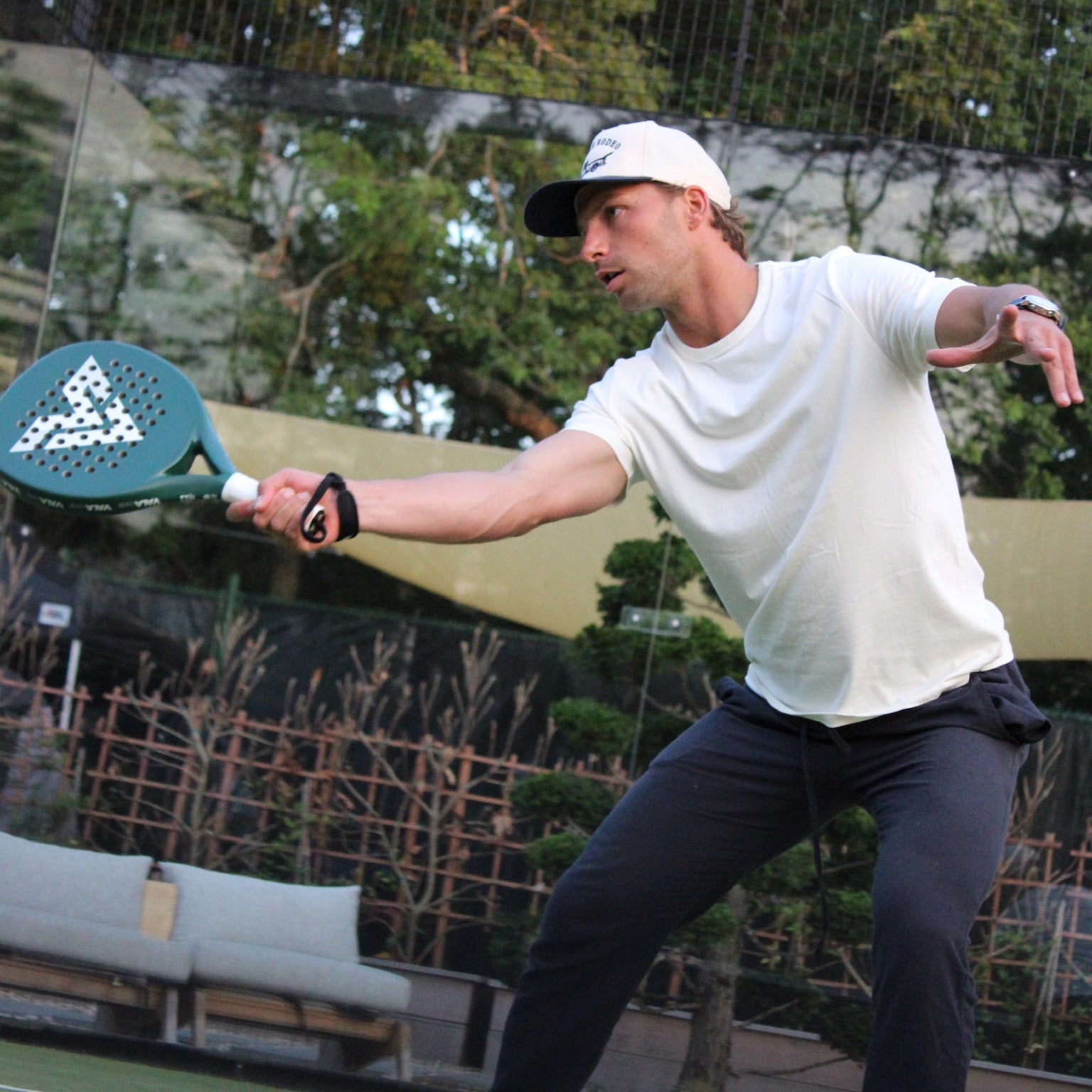 Man playing paddle tennis on a court with trees in the background